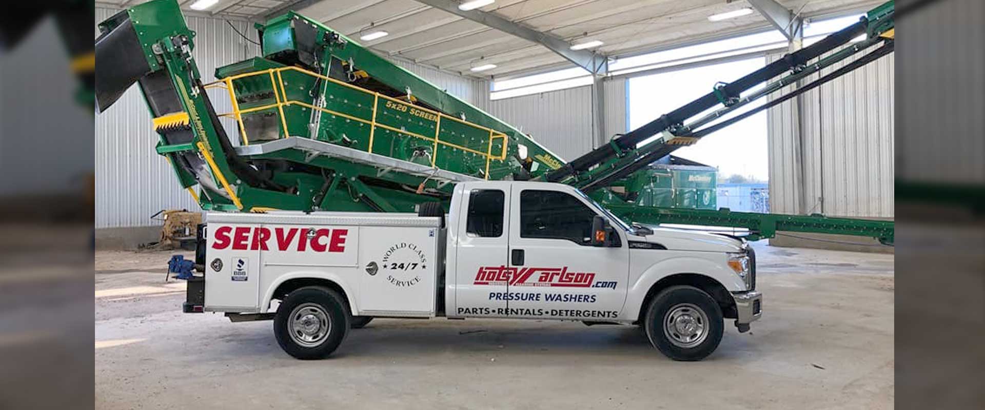Hotsy Carlson 24/7 service truck on-site at an agricultural facility next to a green McCloskey screening plant — pressure washer parts, rentals and detergents for farms